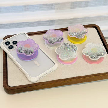 Cute flower-shaped MagSafe phone holder magnetically attached to the back of a white magnetic iPhone case sitting on a wooden tray.