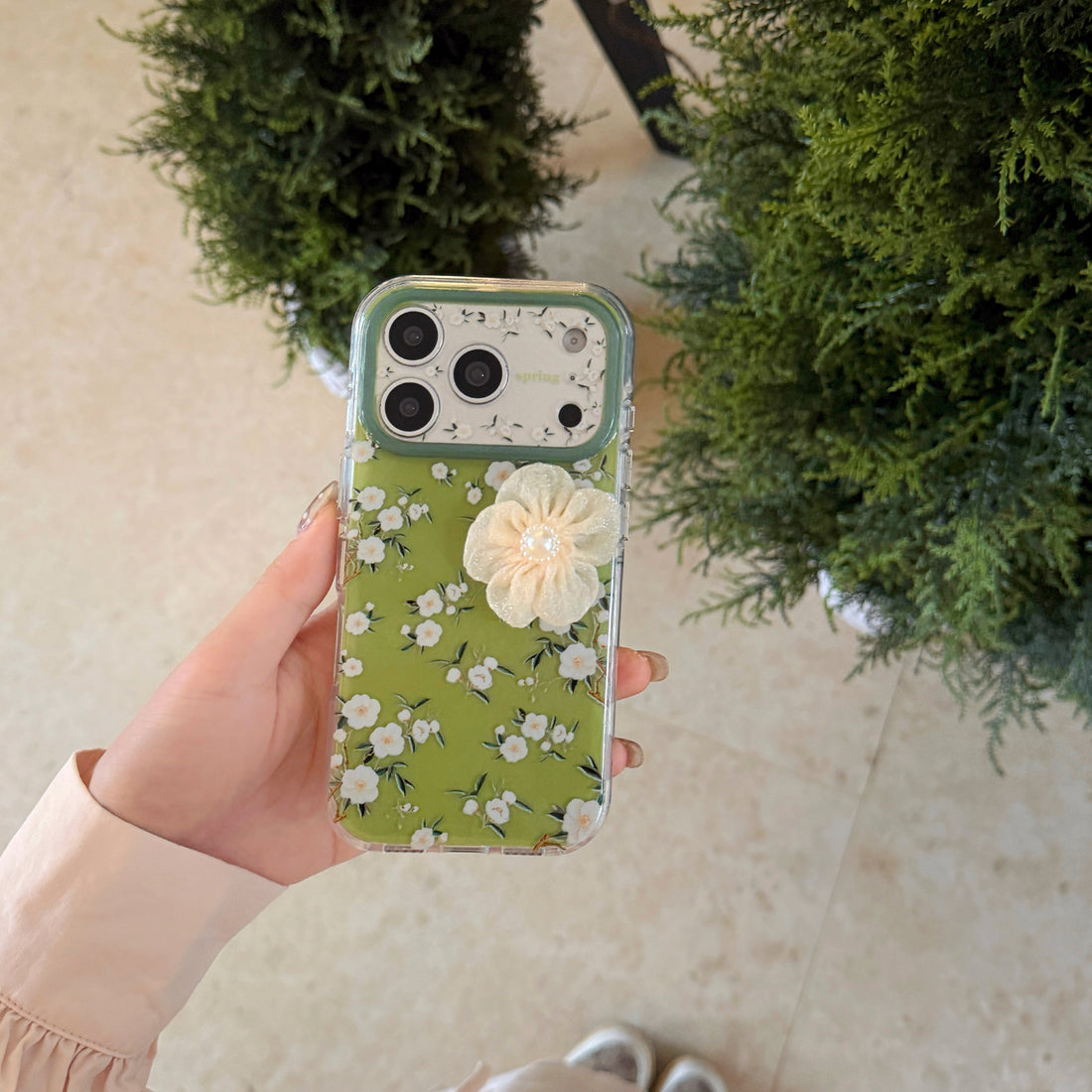iPhone floral phone case with 3D fabric camellia flower decoration and sparkling beaded strap on clear TPU material with avocado green tint, compatible with iPhone 17/16/15 series