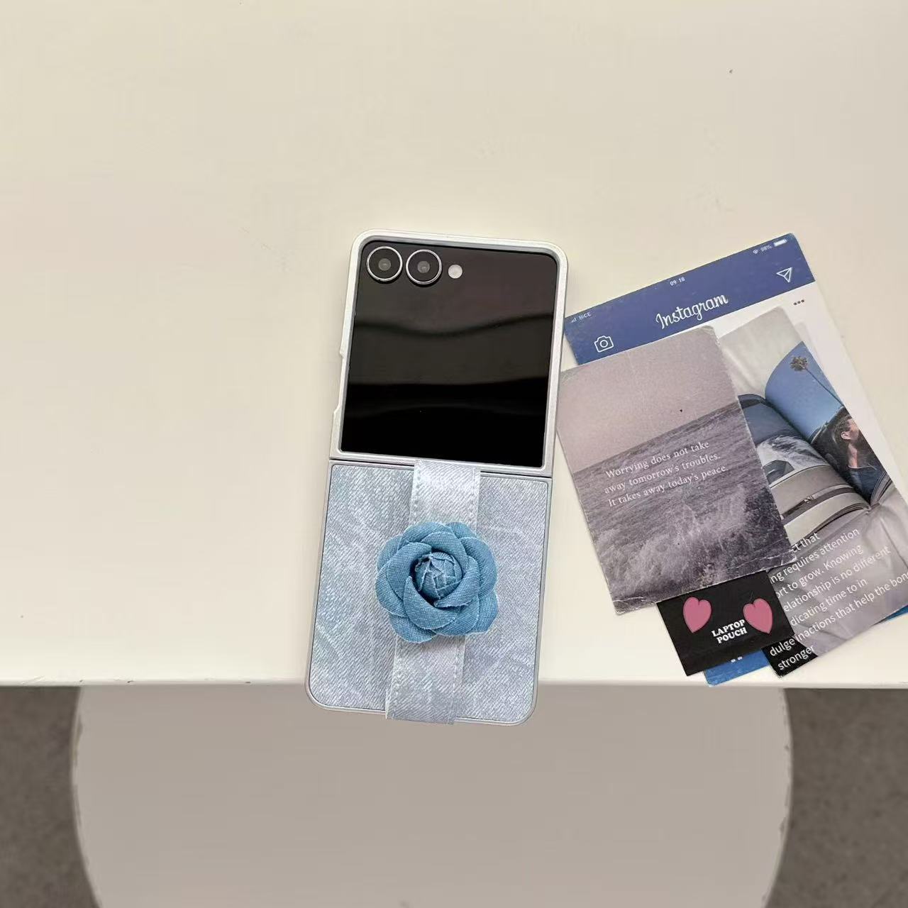 Aesthetic flat lay of Samsung Z Flip 6 denim flower phone case alongside aesthetic photo cards on a neutral table.