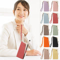A woman holds a pink pebbled leather smartphone wallet case with its matching wrist strap with ten identical closed flip cases in various colors (purple, blue, taupe, green, orange, black, yellow)