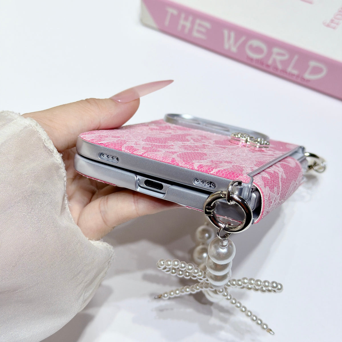 Bottom close-up view of hot pink lace case for iPhone DUO showing precise speaker cutouts, charging port opening, and metal strap rings.