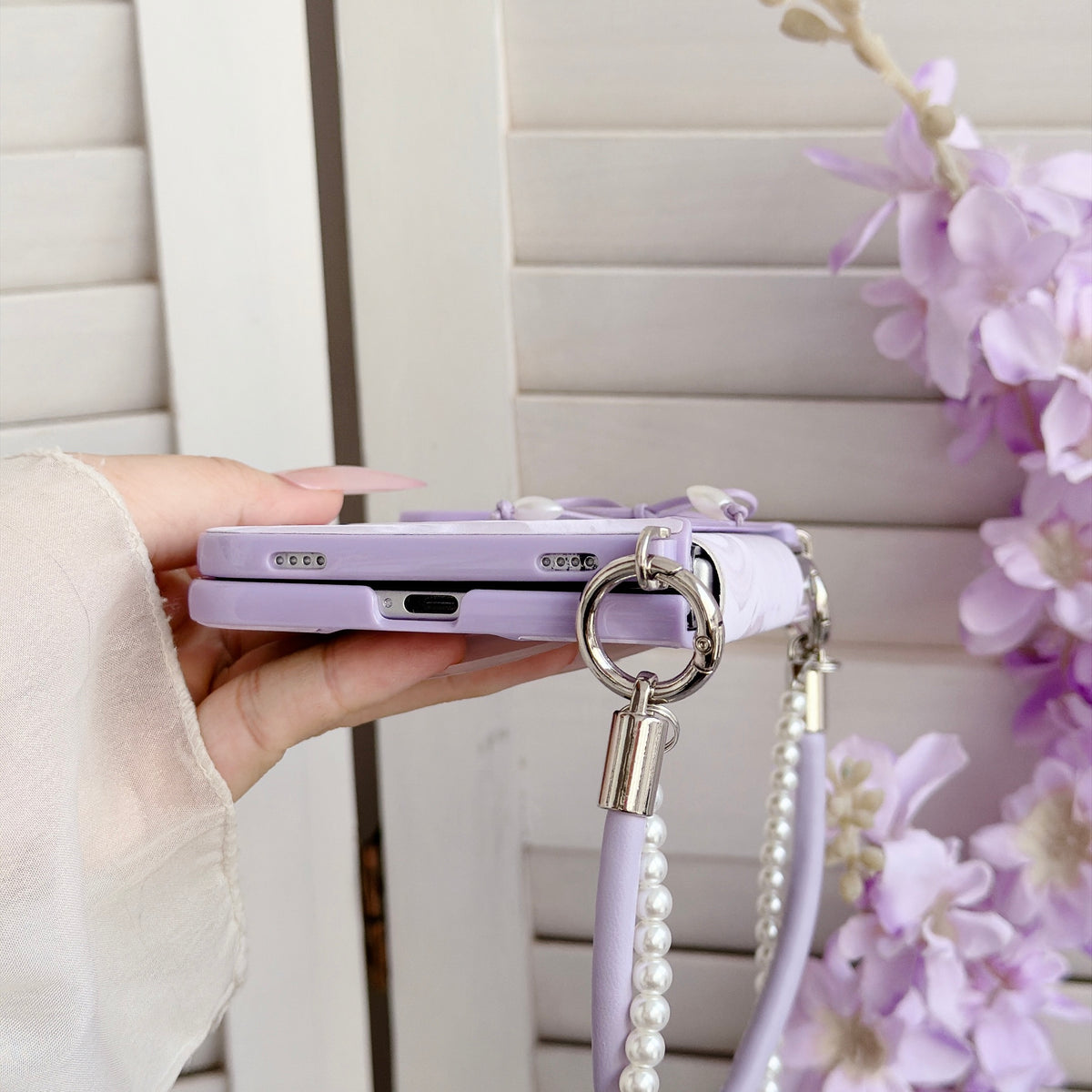 Bottom view close-up of the pastel lavender marble case for iPhone DUO showing precise speaker openings, USB-C charging port cutout, and durable metal attachment rings.