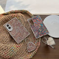 Brown and multi-color paisley tapestry Samsung Galaxy Z Fold 8 cases resting on a woven straw tote bag with attached heart compact mirror charm.