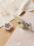 Clear iPhone case supported horizontally on a desk using the yellow flower-star mirror phone grip.