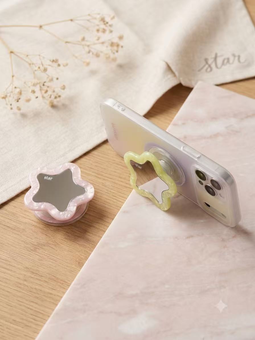 Clear iPhone case supported horizontally on a desk using the yellow flower-star mirror phone grip.