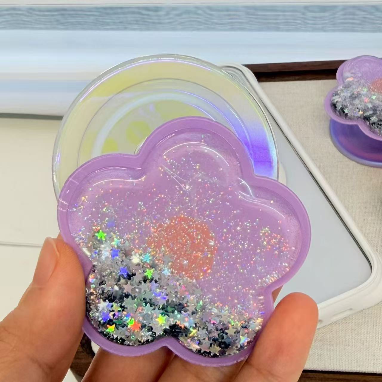 Lavender purple MagSafe glitter flower phone grip magnetically attached to clear iPhone case on wooden tray.