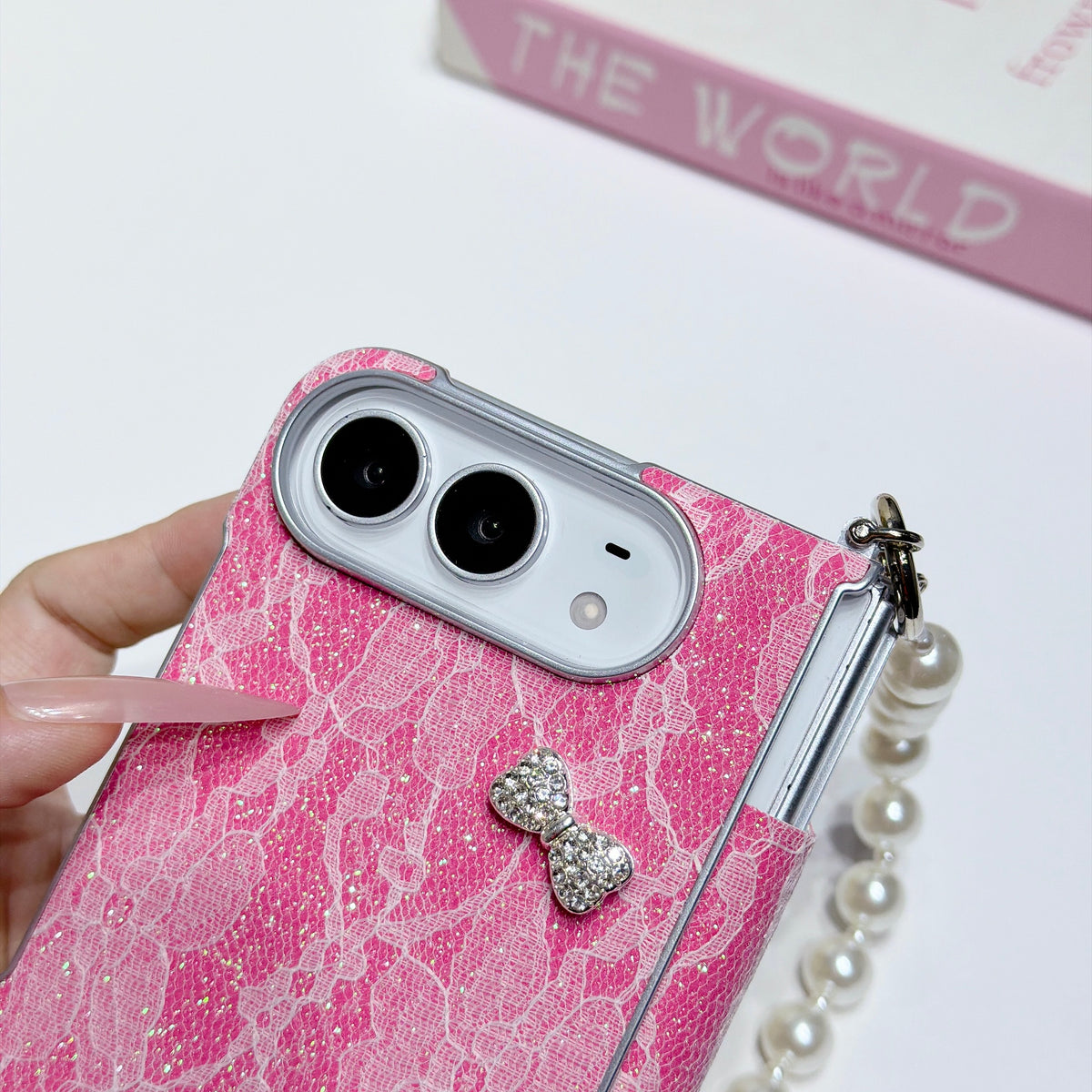 Close-up shot of hot pink glitter lace case for iPhone DUO highlighting raised camera bezel protection ring and crystal rhinestone bow embellishment.