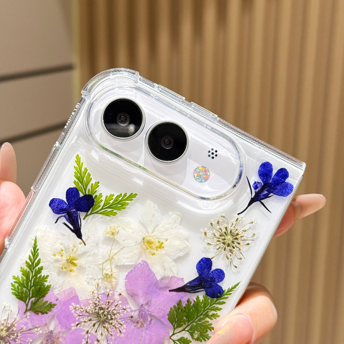 Close-up detail view of the raised camera bezel and dual lens cutouts on the clear iPhone DUO case embedded with real blue and white pressed flowers.