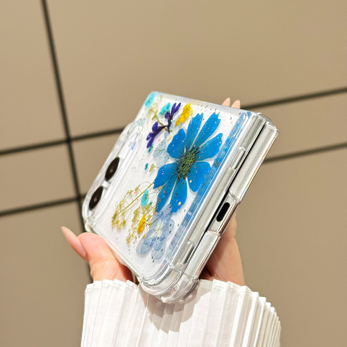 Close-up side perspective of a hand holding the clear iPhone DUO real pressed flower case, highlighting precision hinge alignment, charging port cutout, and protective corner bumpers.
