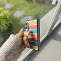 Close-up side profile showing phone hinge, secure hand strap grip, and back camera cutout on rainbow striped Samsung Z Fold case