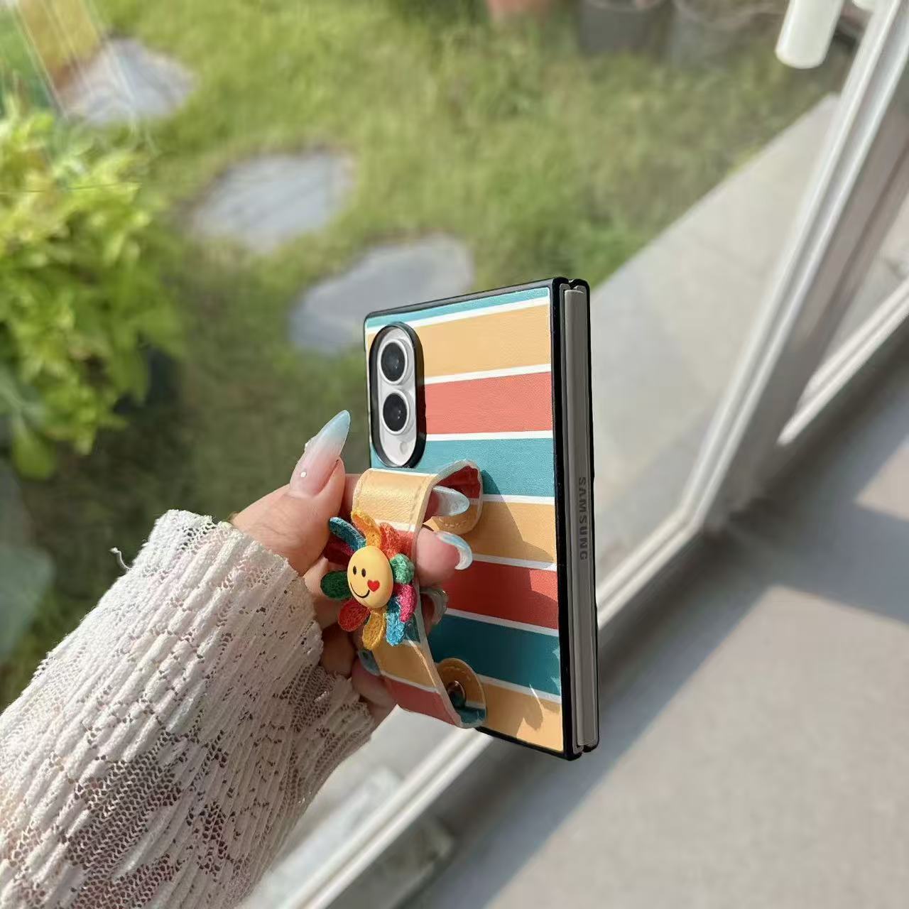 Close-up side profile showing phone hinge, secure hand strap grip, and back camera cutout on rainbow striped Samsung Z Fold case