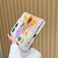 Close-up side view of a hand holding the clear iPhone DUO real pressed flower case at a bottom angle, showing the charging port cutout, precision hinge clearance, and embedded floral garden arrangement.