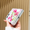 Close-up side view of a hand holding the clear iPhone DUO real pressed flower case at a bottom angle, showing the charging port cutout, precision hinge clearance, and embedded pink floral arrangement.