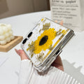 Close-up side view of a hand holding the clear iPhone DUO real pressed flower case at a bottom angle, showing the charging port cutout, precision hinge clearance, and embedded sunflower arrangement.