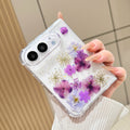 Close-up top perspective of a hand holding the clear iPhone DUO real pressed purple flower case, highlighting fine holographic glitter flecks and rich violet petal tones.