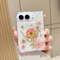 Close-up vertical perspective of a hand holding the clear iPhone DUO real pressed flower case, highlighting holographic star flecks and detailed floral layouts.