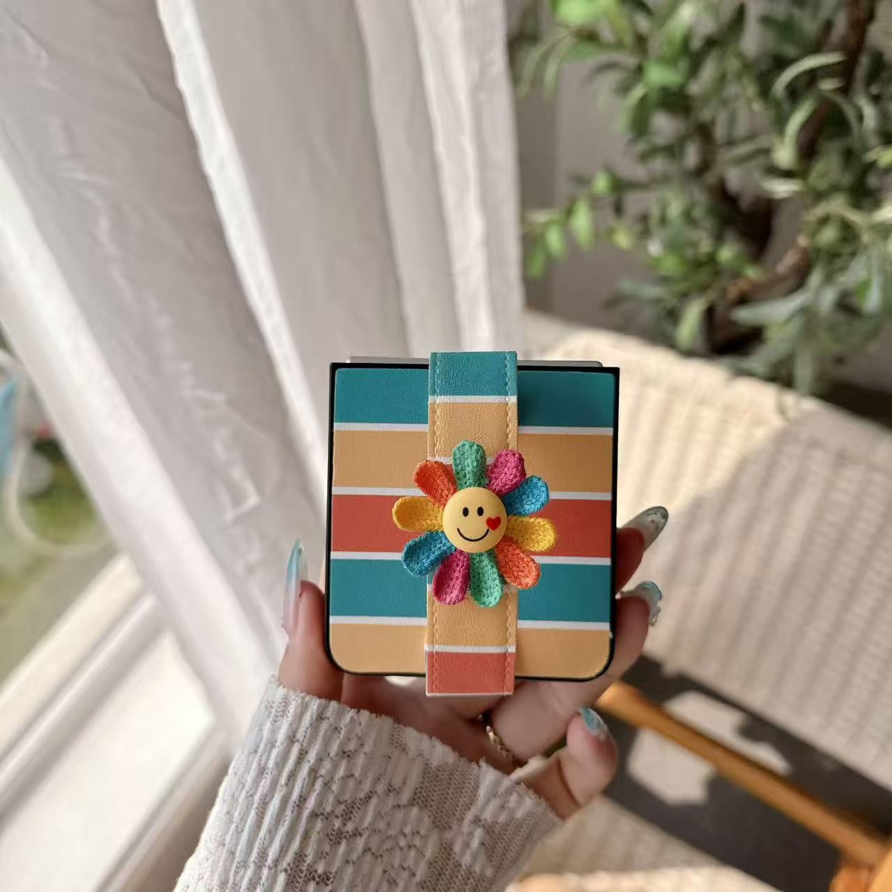 Close-up view of folded Galaxy Z Flip case featuring teal yellow coral stripes and a cute smiling flower charm.⁠