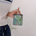 Close-up view of the green paisley fabric pattern phone case with heart compact mirror charm attached to top ring.