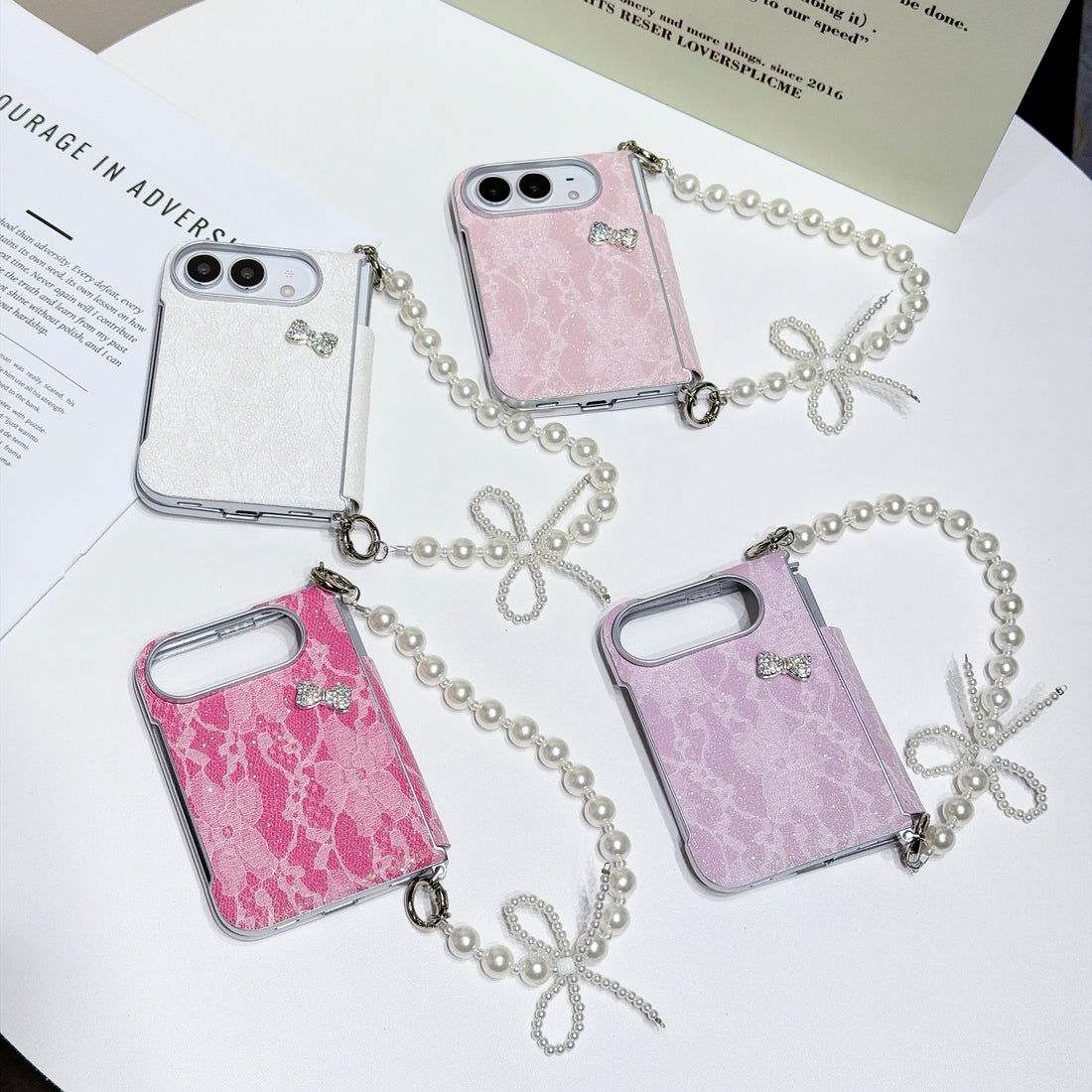 Collection of iPhone DUO lace cases with pearl bow chain straps laid out in four available colors including hot pink, light pink, white, and soft lavender.