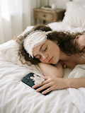 Coquette style aesthetic photo of a woman resting in bed next to a black smartphone with a bunny phone stand