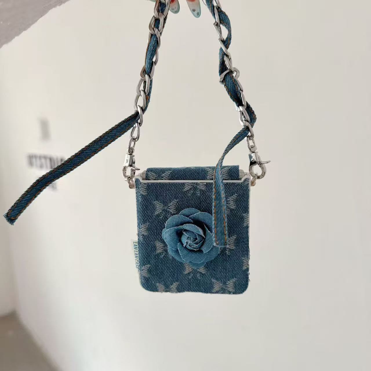 Denim flower Z Flip phone case hanging by its wrist strap against a white background.