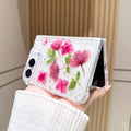 Desk display shot of the iPhone DUO clear case with real pressed pink flowers and silver flakes standing open on a surface.