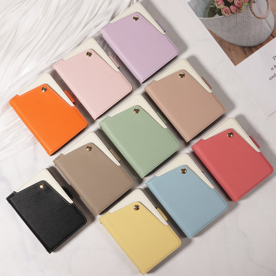 Flat lay view displaying 10 color variations of the dual-tone leather wallet case for iPhone DUO, arranged on a table surface including Black, Orange, Pink, Lavender, Taupe, Sage Green, Red, Yellow, Sky and Beige