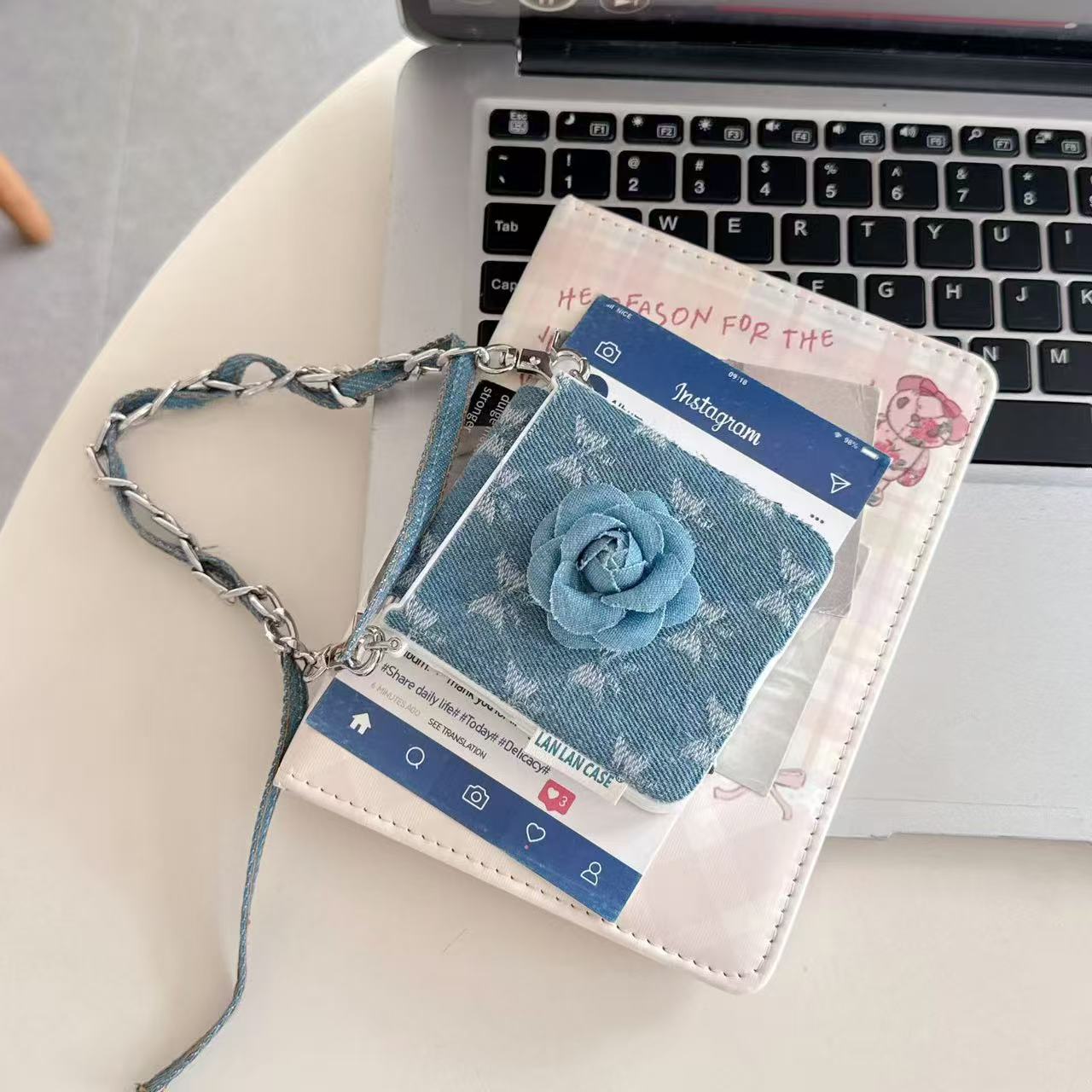 Folded Samsung Z Flip denim floral wristlet case resting on a laptop keyboard alongside aesthetic cards.