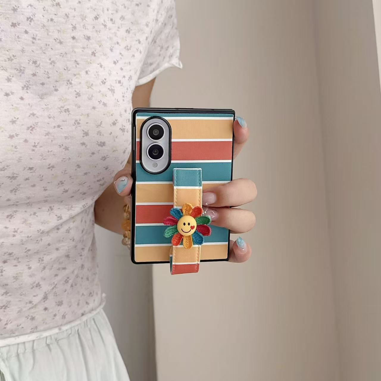 Front view of woman holding a Samsung Galaxy Z Fold case with vintage stripe pattern and colorful crocheted smiley face flower grip