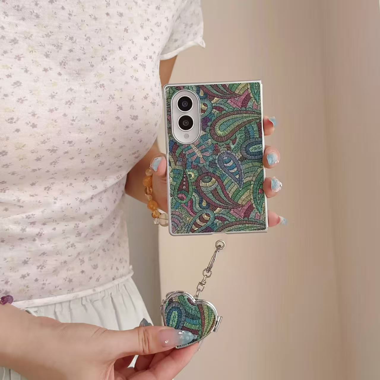 Hand holding a green and pink paisley tapestry Samsung Galaxy Z Fold 8 case with dangling heart charm.