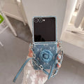 Folded Samsung Z Flip denim floral wristlet case resting on a laptop keyboard alongside aesthetic cards.
