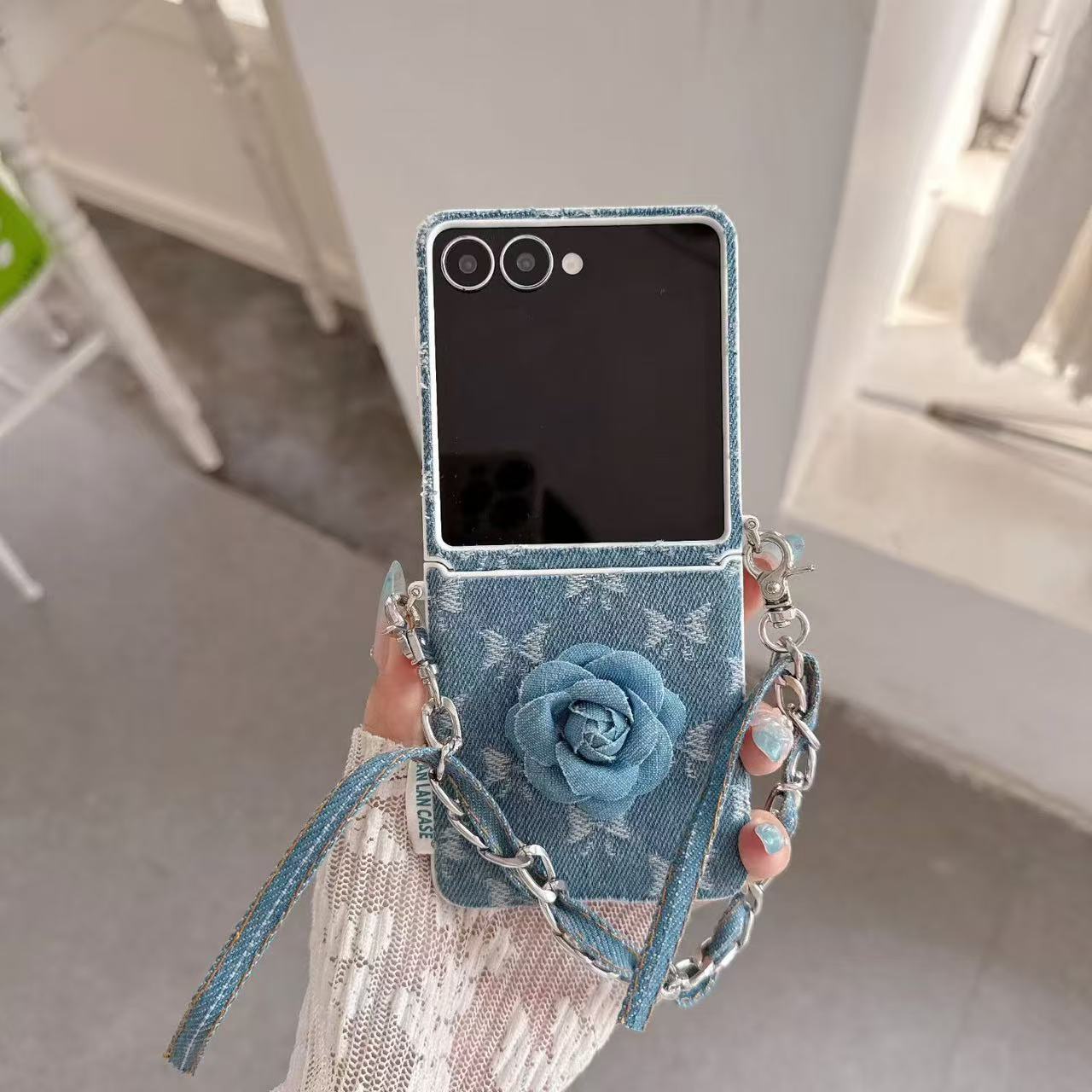 Folded Samsung Z Flip denim floral wristlet case resting on a laptop keyboard alongside aesthetic cards.