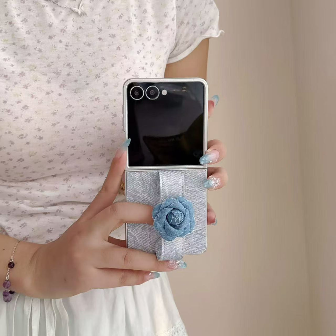 Hand holding unfolded Samsung Galaxy Z Flip wearing a light blue denim floral strap case.