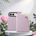 Lavender purple dual-tone leather wallet case for iPhone DUO displayed on a marble pedestal next to pink flowers.