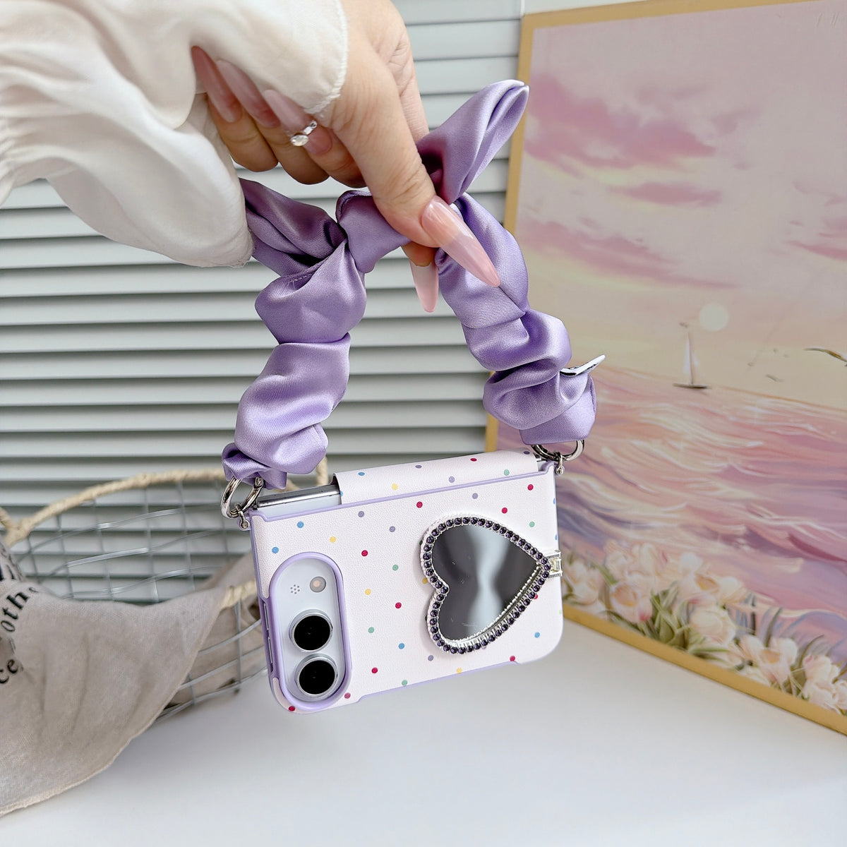 Lavender purple polka dot iPhone DUO case hanging vertically from a hand by its soft satin scrunchie bow wristlet strap.