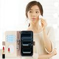 Lifestyle overlay showing a woman applying makeup while demonstrating the opened dual-tone leather wallet case for iPhone, featuring three interior credit card slots, a cash pocket, and a built-in mirror.