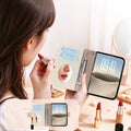 Lifestyle view of a woman applying lipstick while using the built-in vanity mirror inside the dual-tone leather wallet case for iPhone DUO, featuring credit card slots, cash pocket, and screen cover.