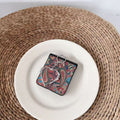 Multi-color boho paisley pattern Samsung Z Flip case with heart charm lying flat on a white ceramic plate.