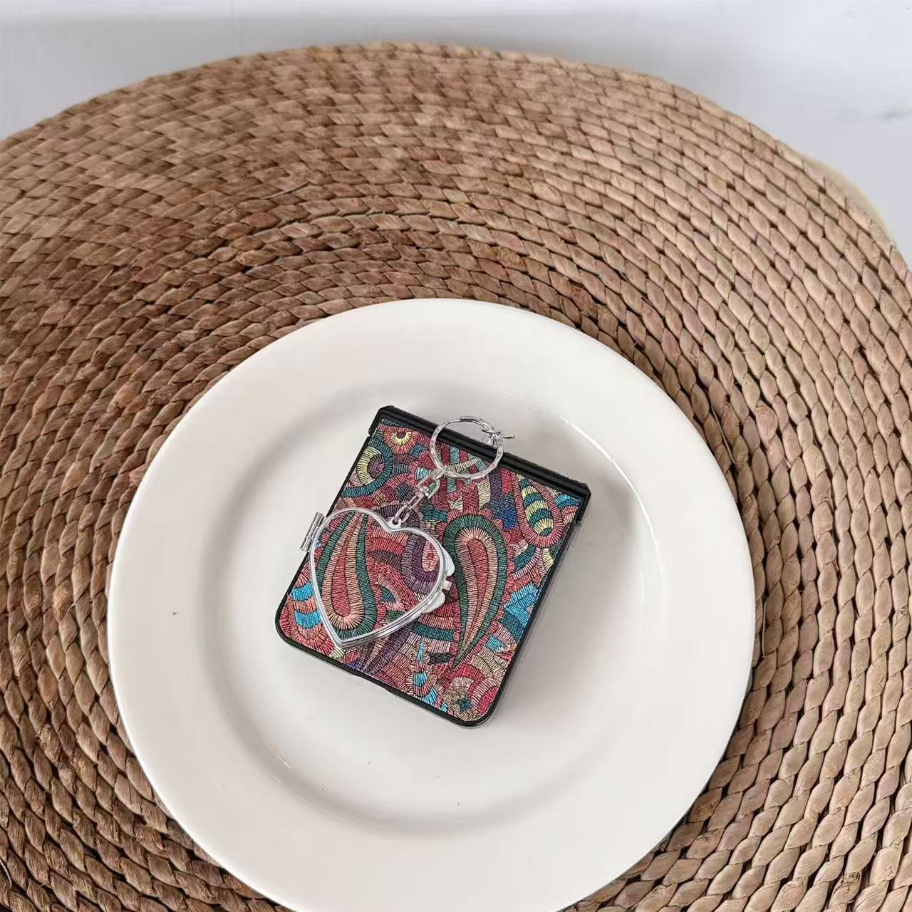 Multi-color boho paisley pattern Samsung Z Flip case with heart charm lying flat on a white ceramic plate.