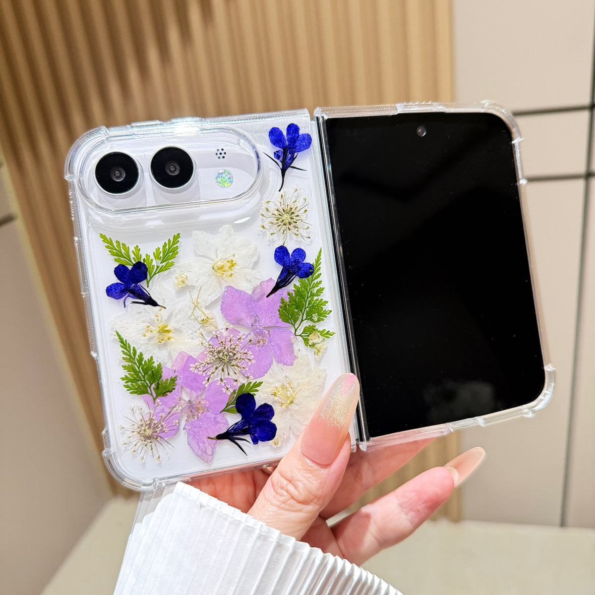 Open view of a hand holding the clear iPhone DUO case showcasing the full real pressed flower garden arrangement alongside the main display screen.