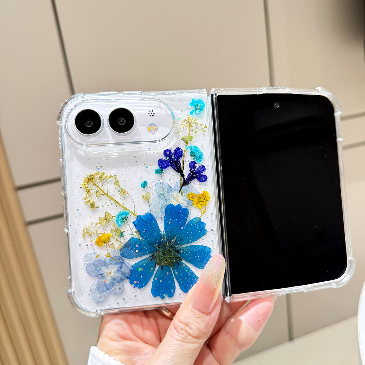 Open view of a hand holding the clear iPhone DUO case showcasing the full real pressed flower royal blue blossom arrangement alongside the main display screen.