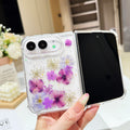 Open view of a hand holding the clear iPhone DUO case showcasing the full real pressed purple flower arrangement alongside the active display screen.