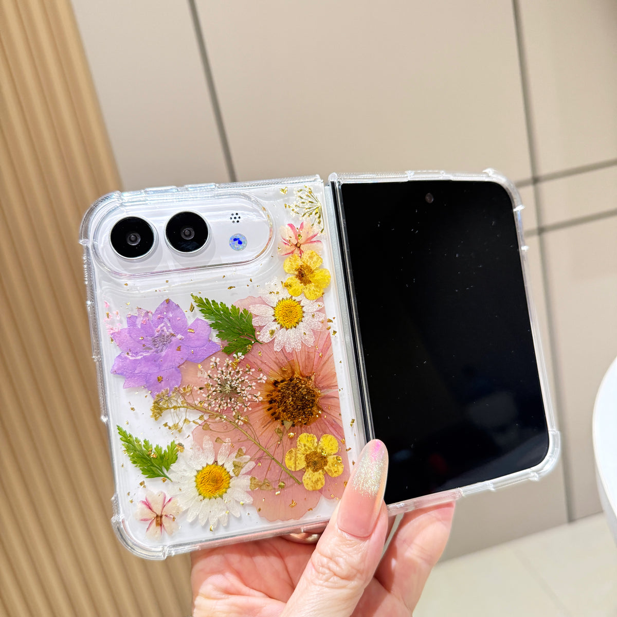 Open view of a hand holding the clear iPhone DUO case showcasing the full real pressed tulip and wildflower arrangement alongside the active display screen.