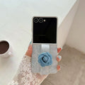 Overhead shot of hand slipping fingers through the blue denim flower strap of a folded Samsung Galaxy Z Flip case.