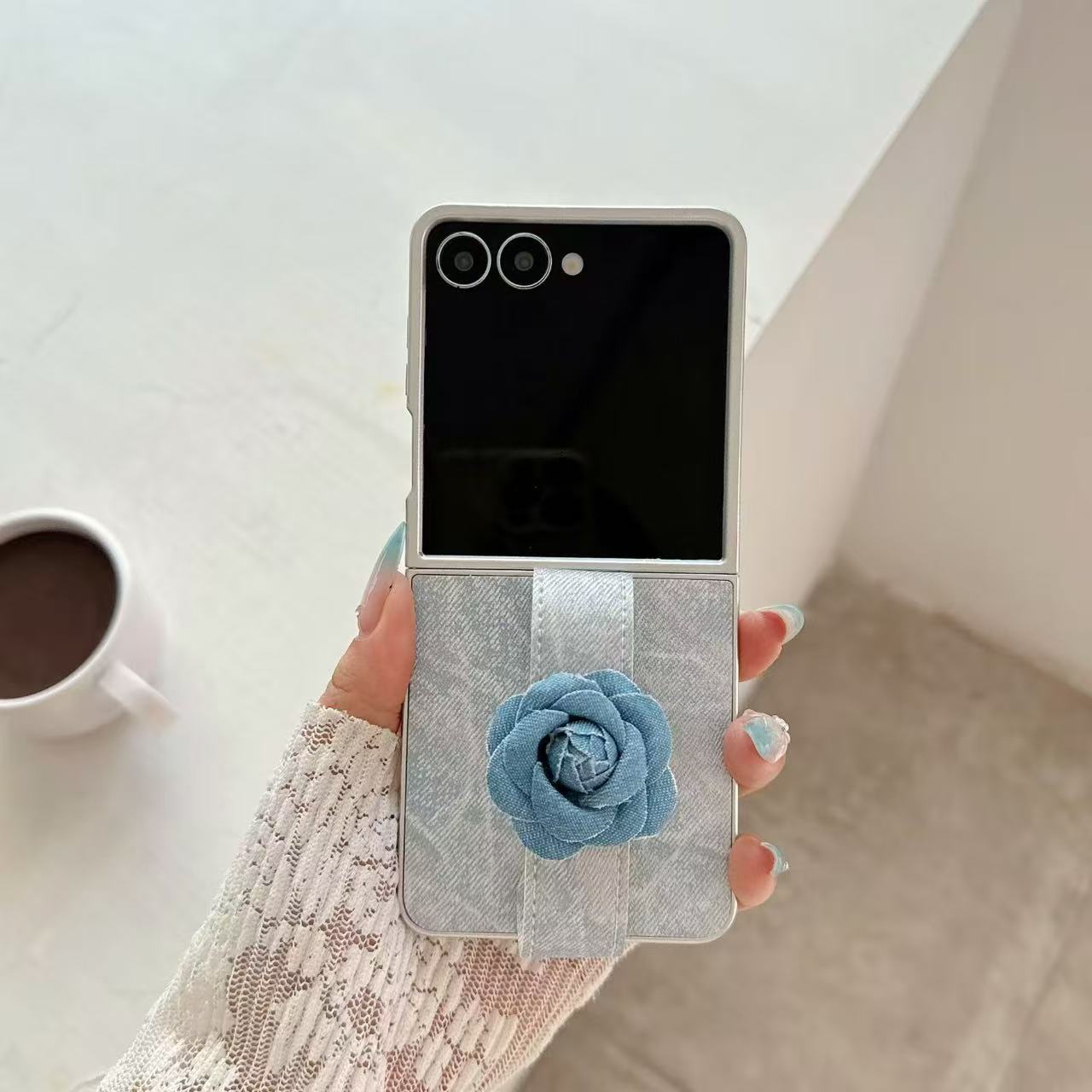 Overhead shot of hand slipping fingers through the blue denim flower strap of a folded Samsung Galaxy Z Flip case.