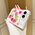 Perspective view of a hand holding the clear pink pressed flower case for iPhone DUO, showing raised camera bezel protection and corner bumper frame.