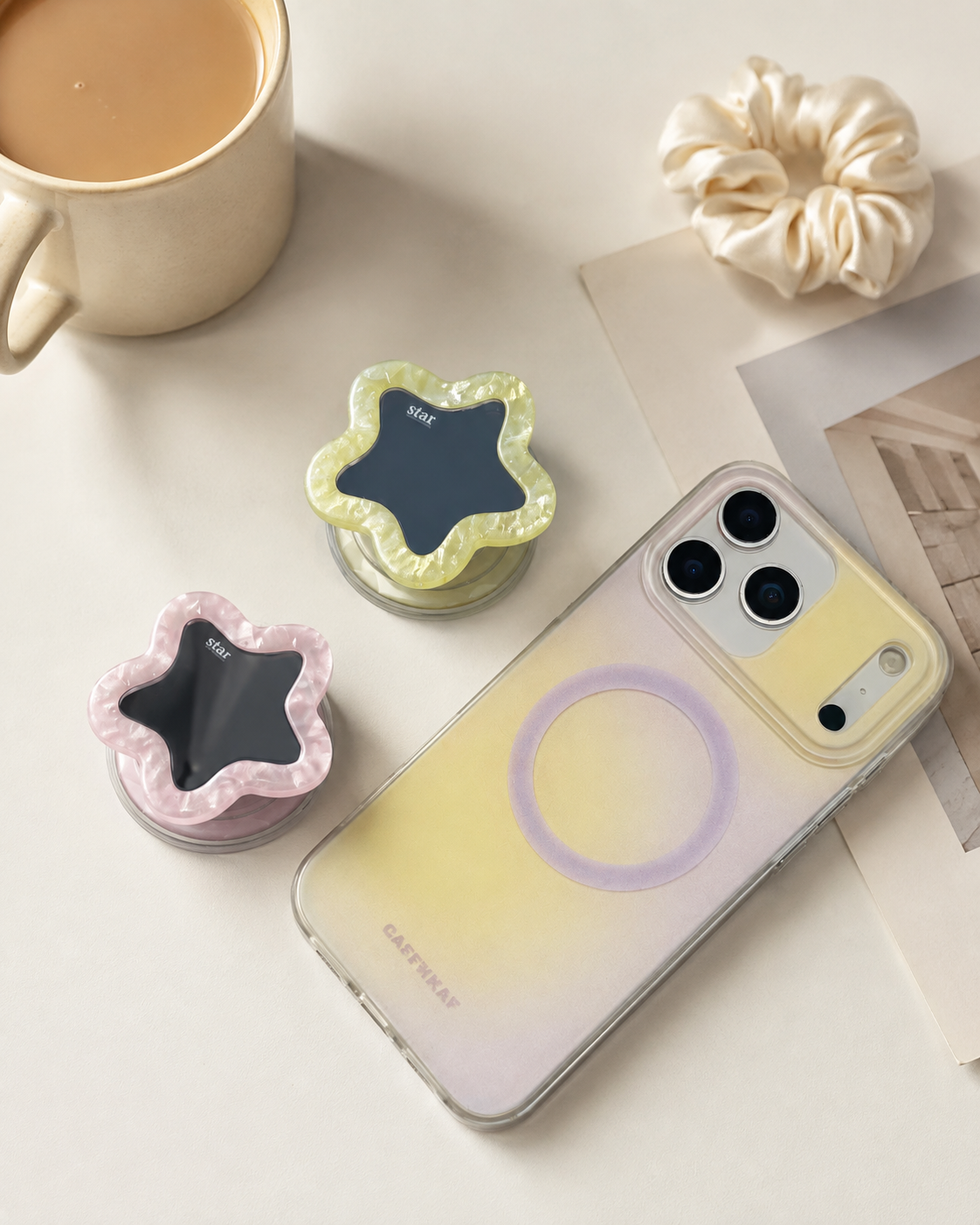 Pink and creamy yellow star mirror phone grips popped out as kickstand next to MagSafe compatible iPhone — expandable phone grip with built-in mirror, aesthetic desk setup

