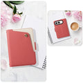 Red dual-tone leather wallet cover for iPhone DUO lying on a notebook next to pink peonies and a coffee cup, showing camera cutout and front cover.