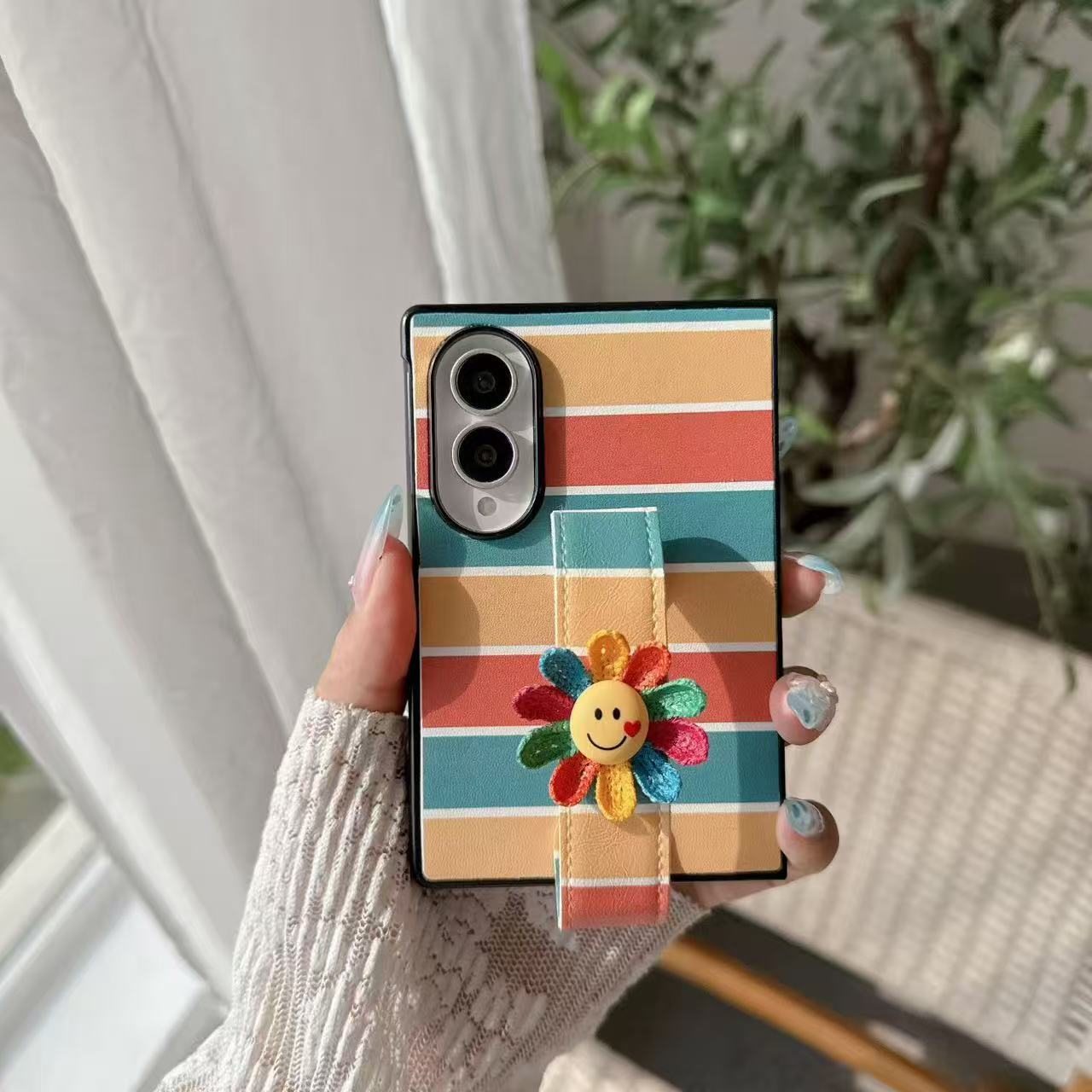 Retro rainbow striped leather phone case for Samsung Galaxy Z Fold featuring built-in smiley flower grip strap held in hand