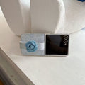 Samsung Galaxy Z Flip resting on a table in flex mode protected by a light blue denim flower strap cover.
